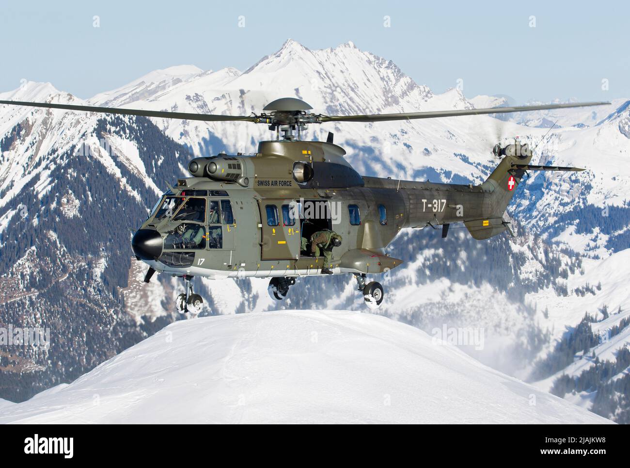A Swiss Air Force AS332 Super Puma helicopter preparing to land on a snowy peak in the Swiss Alps. Stock Photo