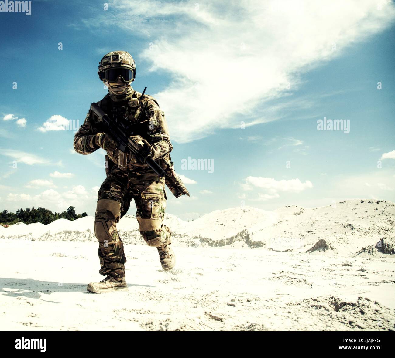 Serviceman running with service rifle in sandy area during military operation. Stock Photo