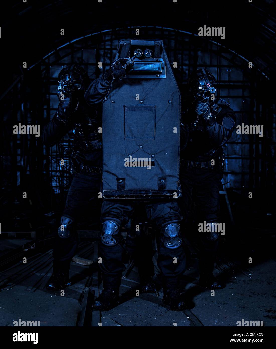 SWAT team members hiding behind ballistic shield, aiming their weapons. Stock Photo