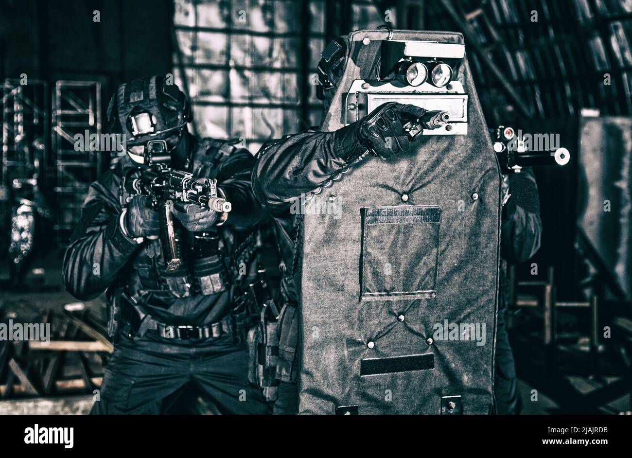 SWAT team officers aiming their weapons while hiding behind ballistic shield during a close quarters situation. Stock Photo