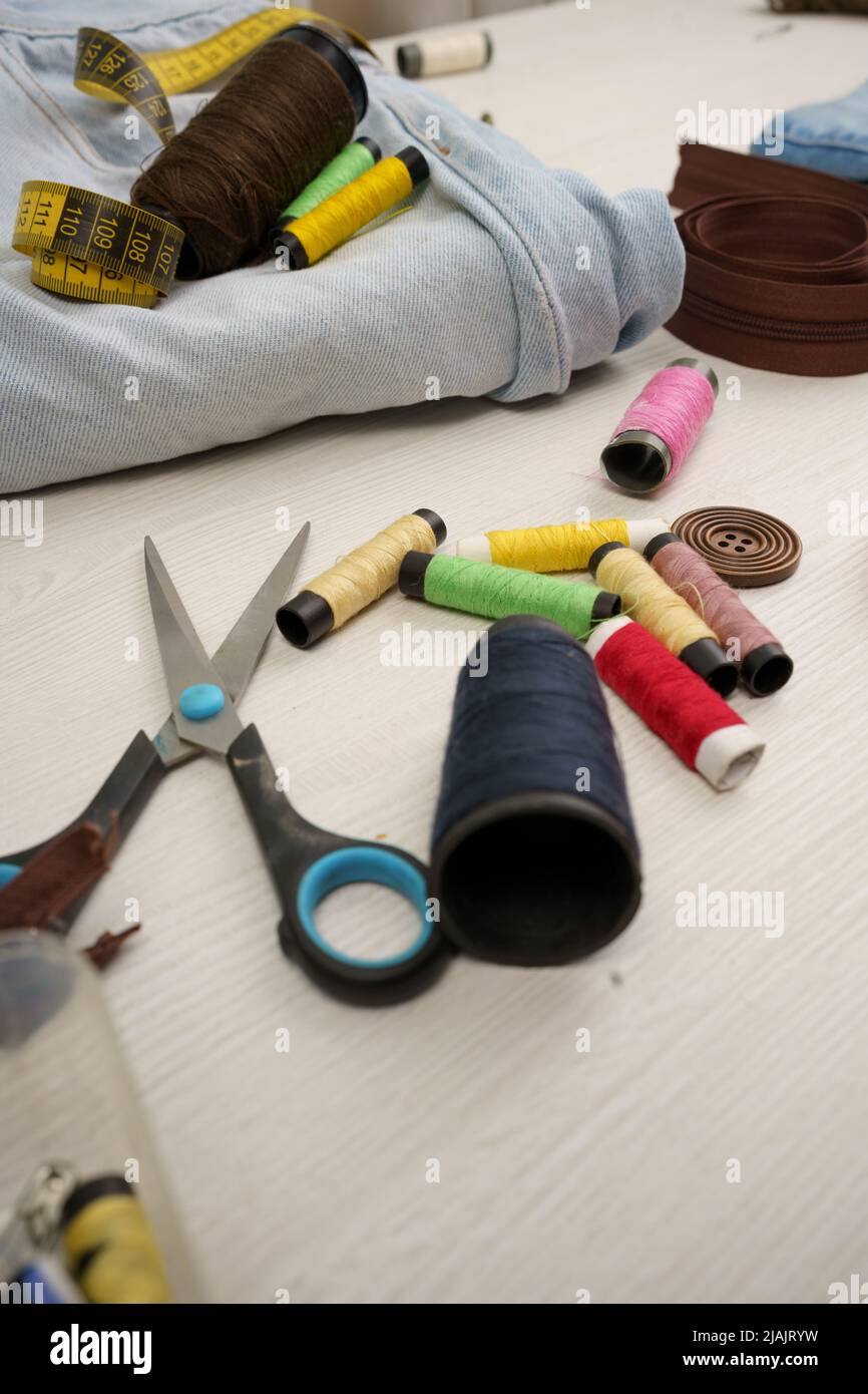 work table with colored threads, scissors, fabric and tape measure, sewing workshop with instruments, detail of objects in studio Stock Photo