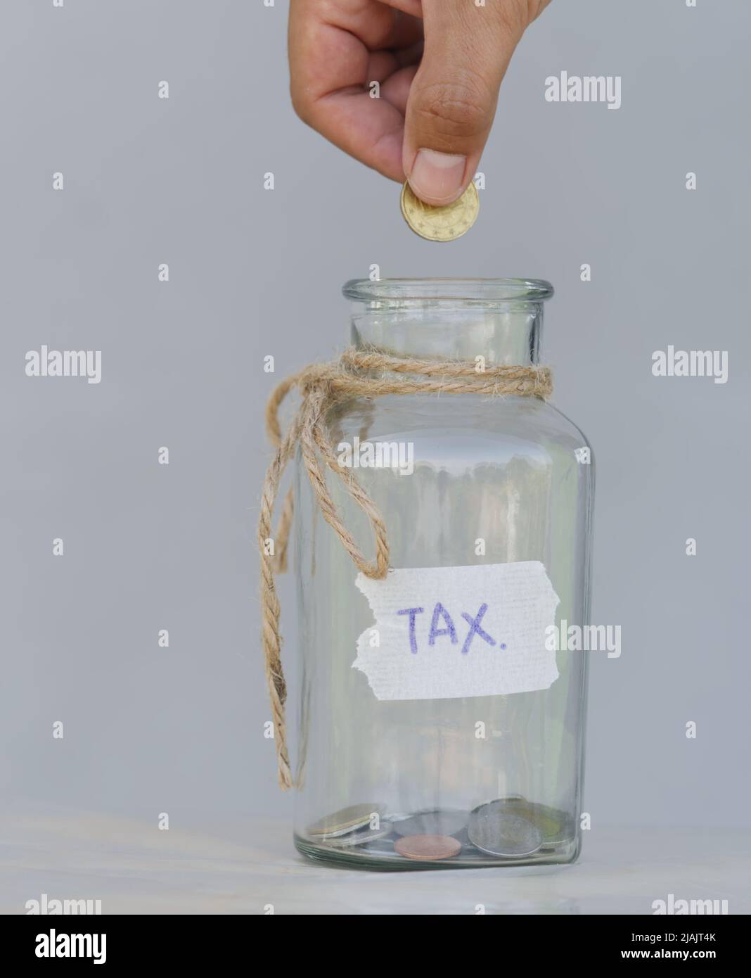Hand putting coin in a glass jar with coins on white background