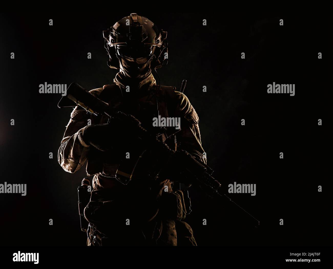 Low key studio portrait of an Army special forces elite soldier standing with assault rifle in darkness. Stock Photo