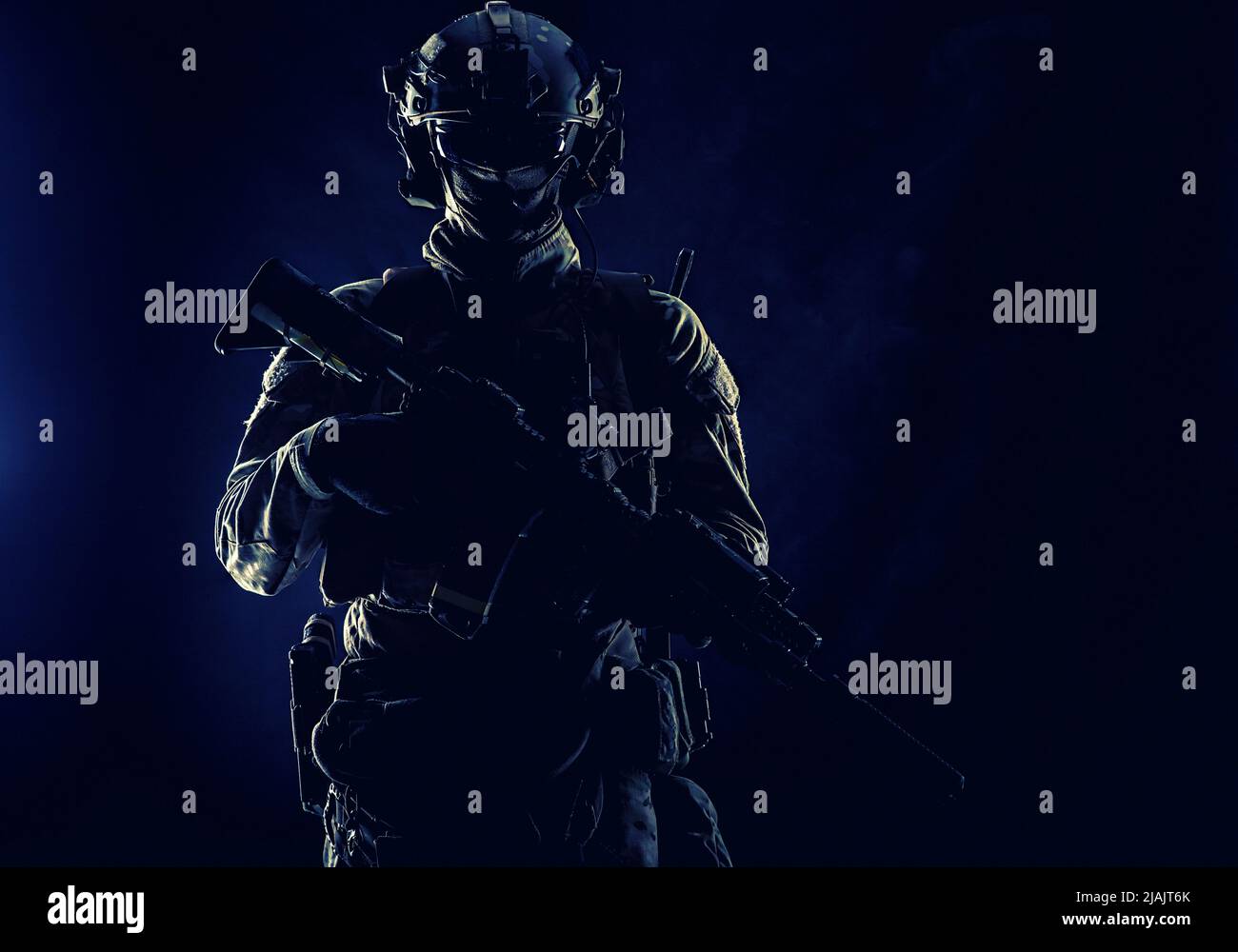 Low key studio portrait of an Army special forces elite soldier standing with assault rifle in darkness. Stock Photo