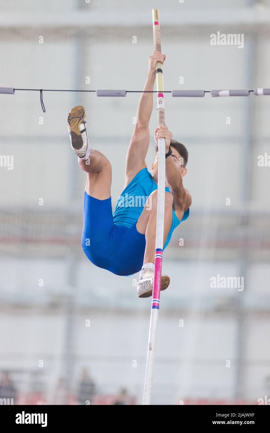 Pole vaulting indoors young man jumping over the partition Stock