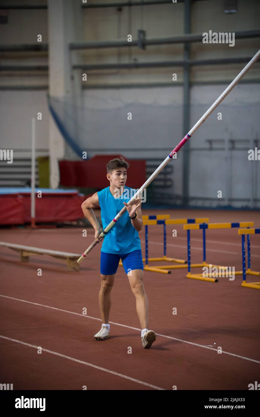Pole vaulting indoors young man standing on the runway holding a pole