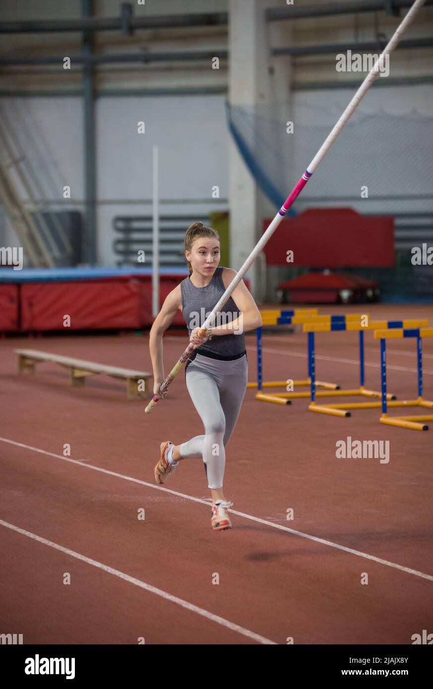 Pole vaulting indoors young sportive woman running on the runway with