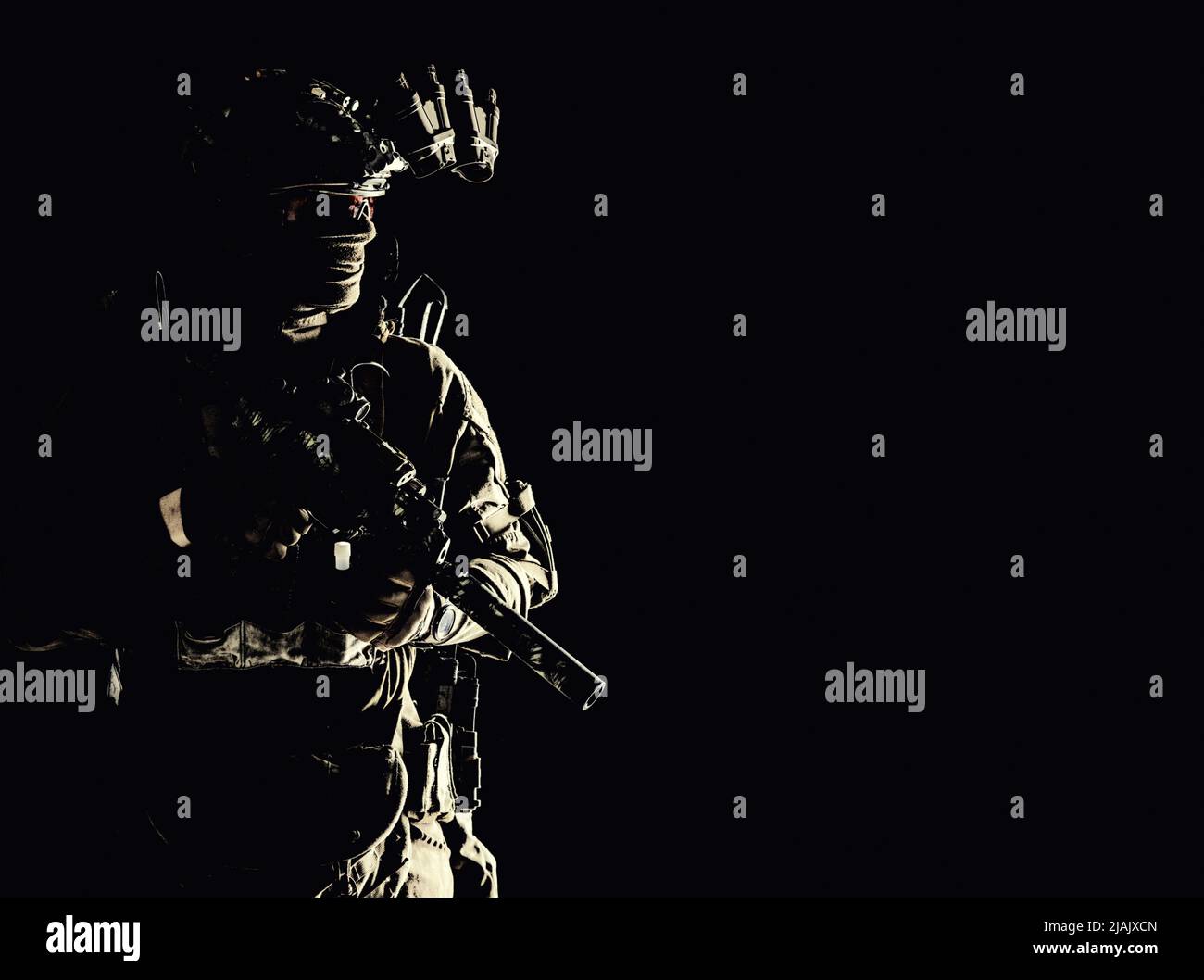 Special forces soldier equipped with night vision device and submachine gun with silencer, looking away. Stock Photo