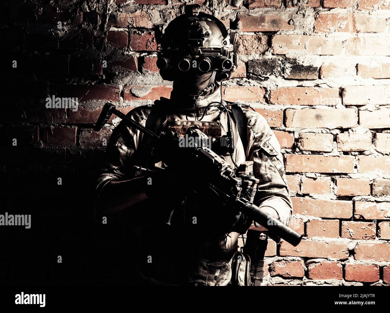 Special forces fighter standing against a brick wall, armed with