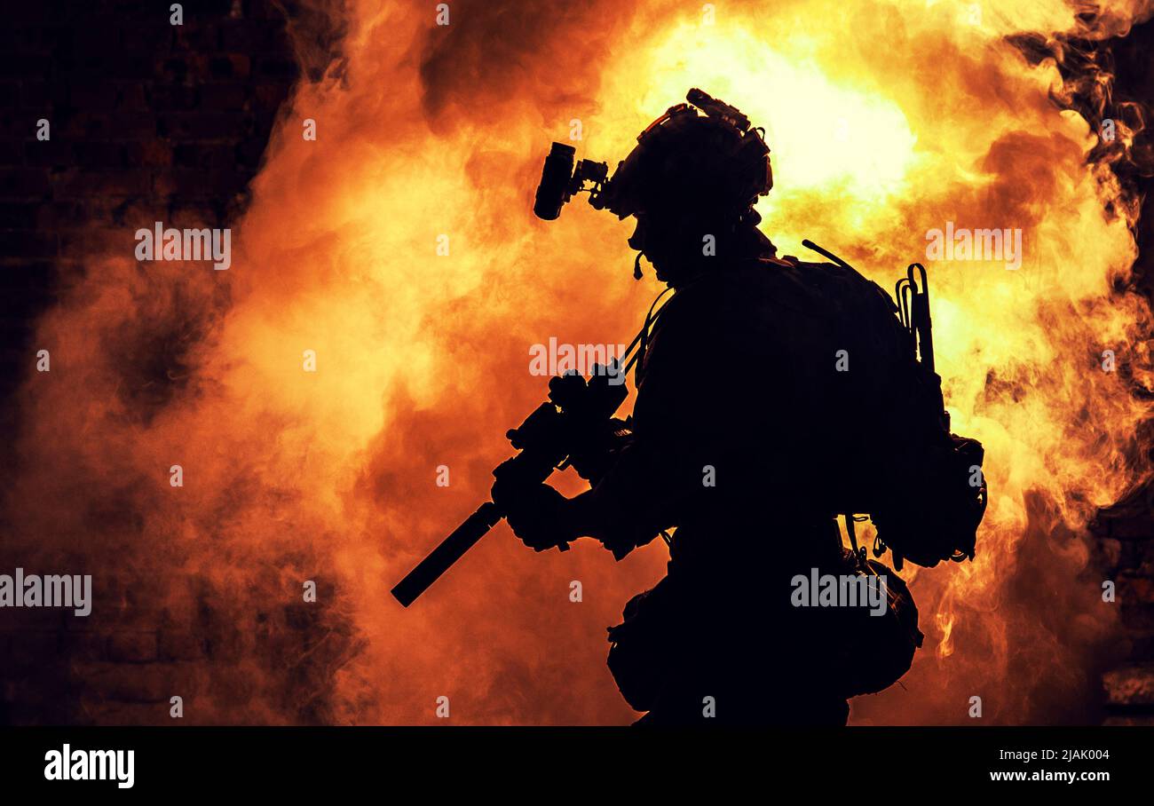 Silhouette of a soldier standing amongst smoke, armed with an assault rifle. Stock Photo