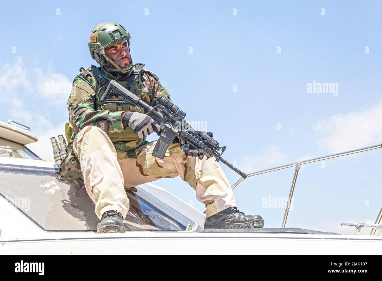 Navy SEALs fighter sitting on the bow of a speed boat with service rifle in hand. Stock Photo