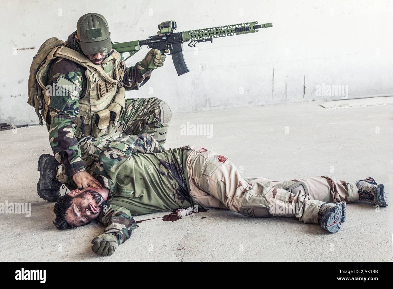 Soldier checking the pulse of an unconscious comrade lying on the floor after being shot in the stomach. Stock Photo