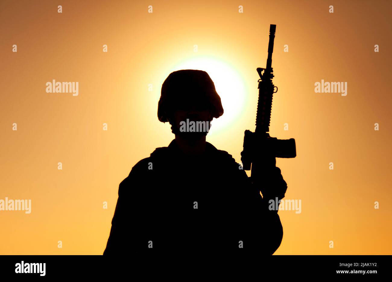 Silhouette of a soldier standing with assault rifle in hand against a ...