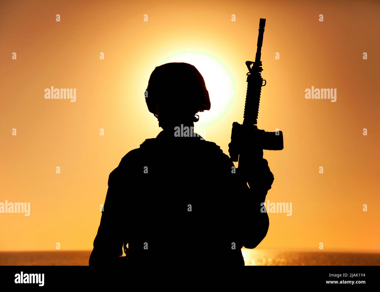Silhouette of a soldier standing with assault rifle in hand against a ...
