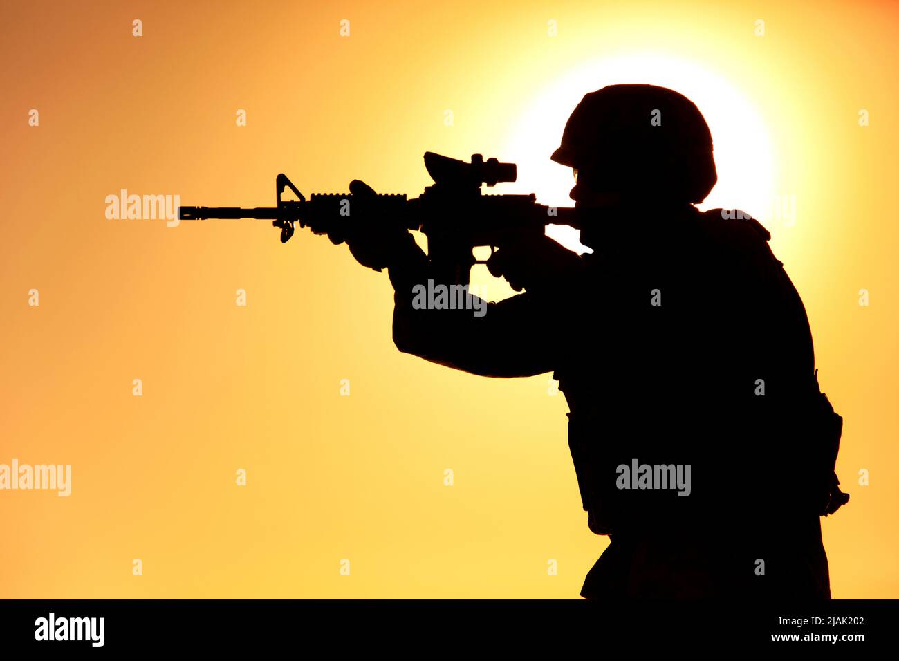 Silhouette of a soldier shooting assault rifle against a sunlit night sky. Stock Photo