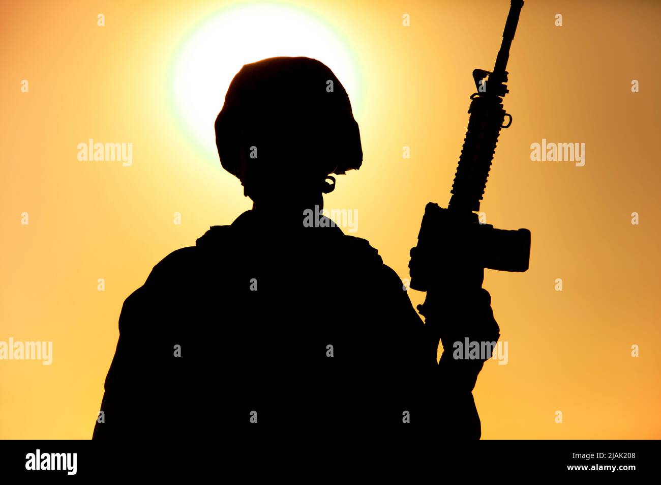 Silhouette of a soldier standing with assault rifle in hand against a ...