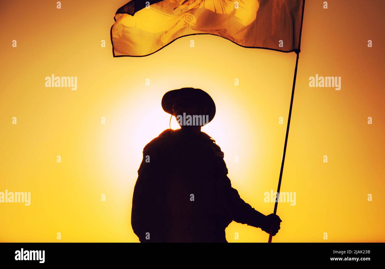 Silhouette of a soldier waving flag against a sunset sky. Stock Photo