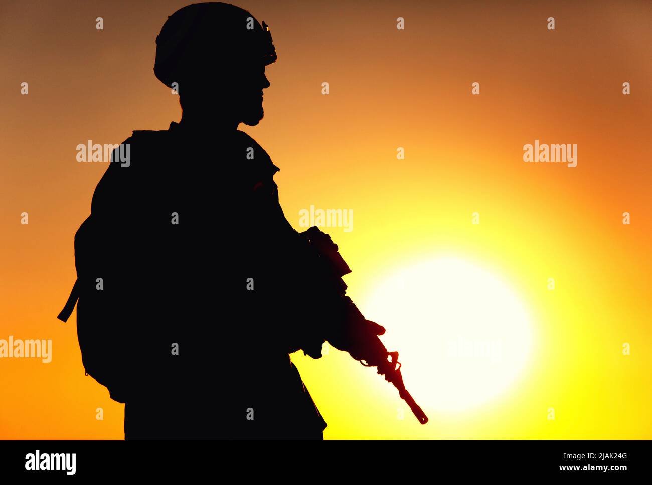 Silhouette of rifleman carrying tactical backpack and service rifle, with background of sunset sky. Stock Photo