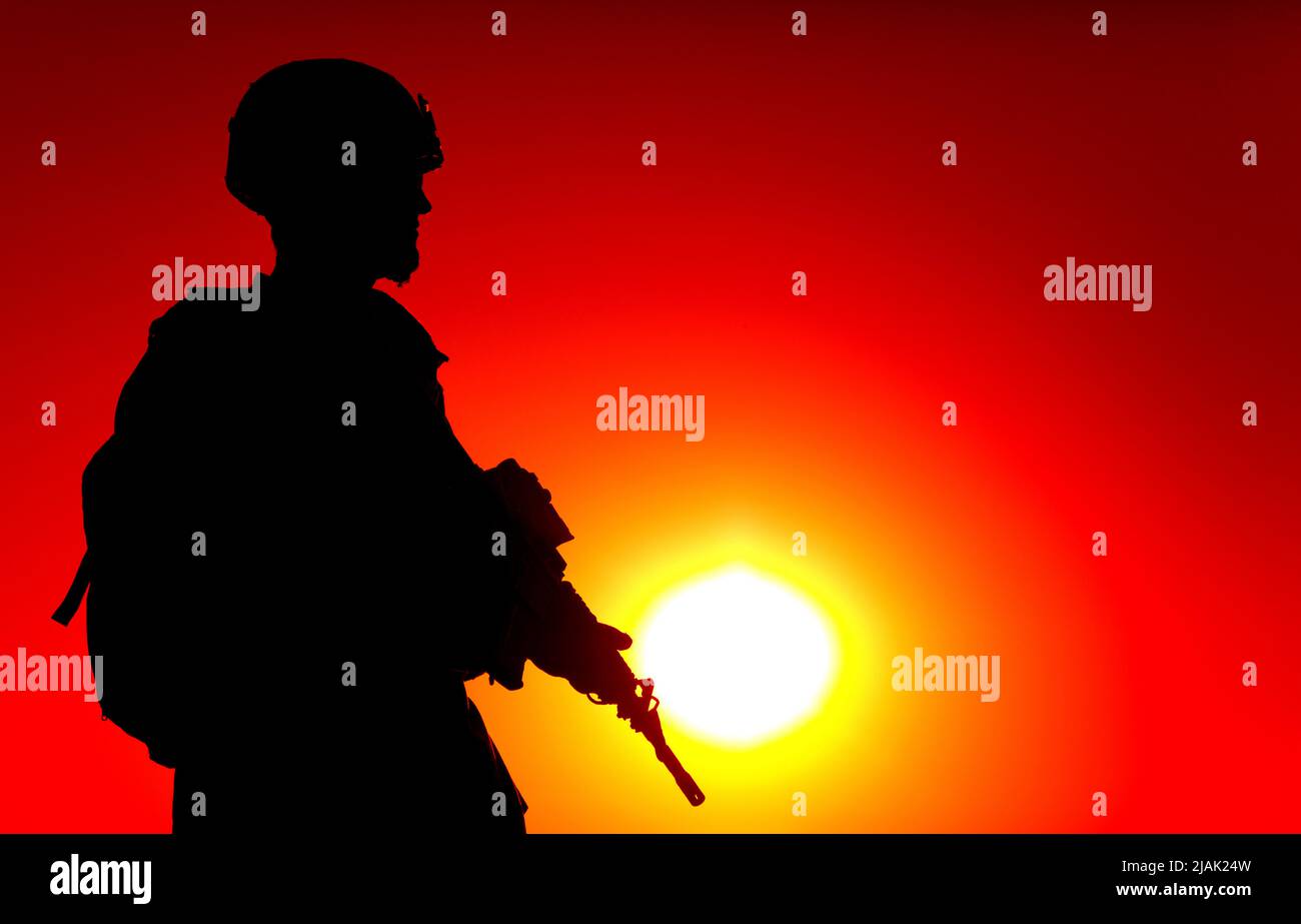 Silhouette of rifleman standing on ocean coastline, patrolling at sunset. Stock Photo