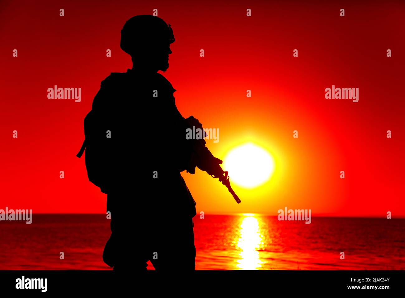 Silhouette of rifleman standing on ocean coastline, patrolling at sunset. Stock Photo