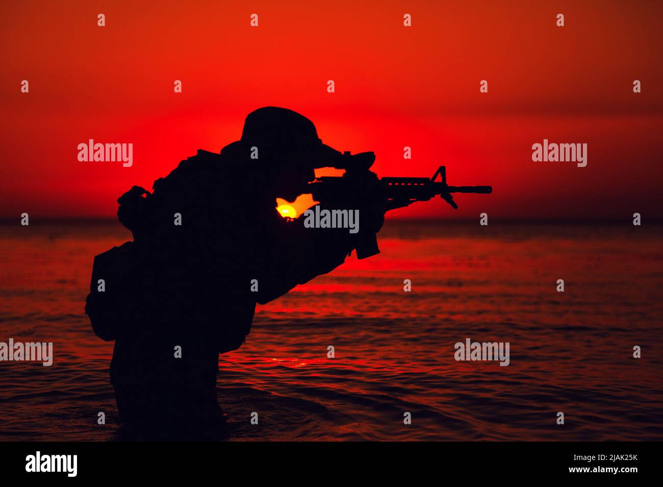 Silhouette of a soldier shooting rifle while standing knee deep in water. Stock Photo