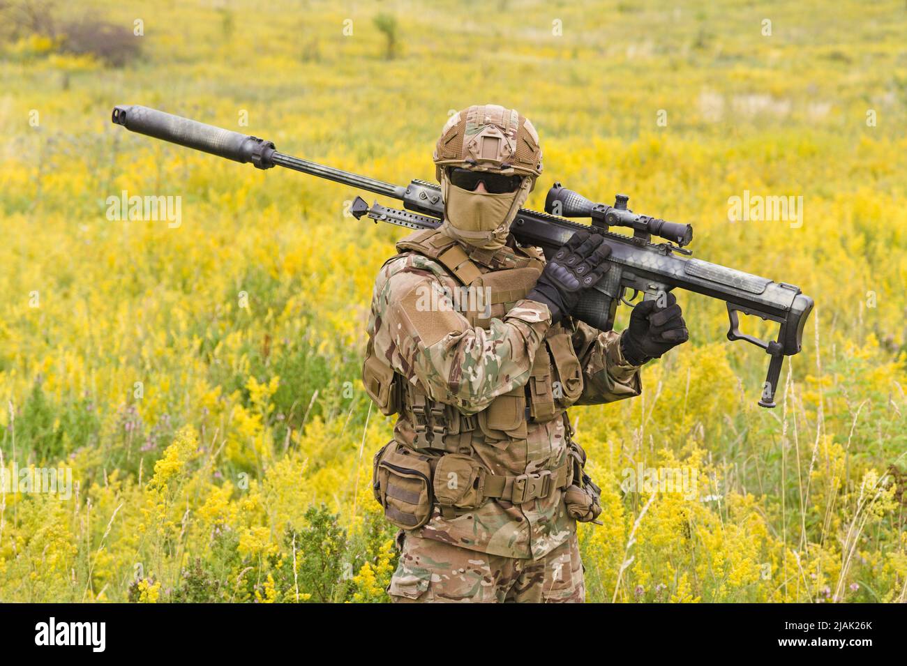 Soldier with big sniper rifle walking across blooming field. Stock Photo