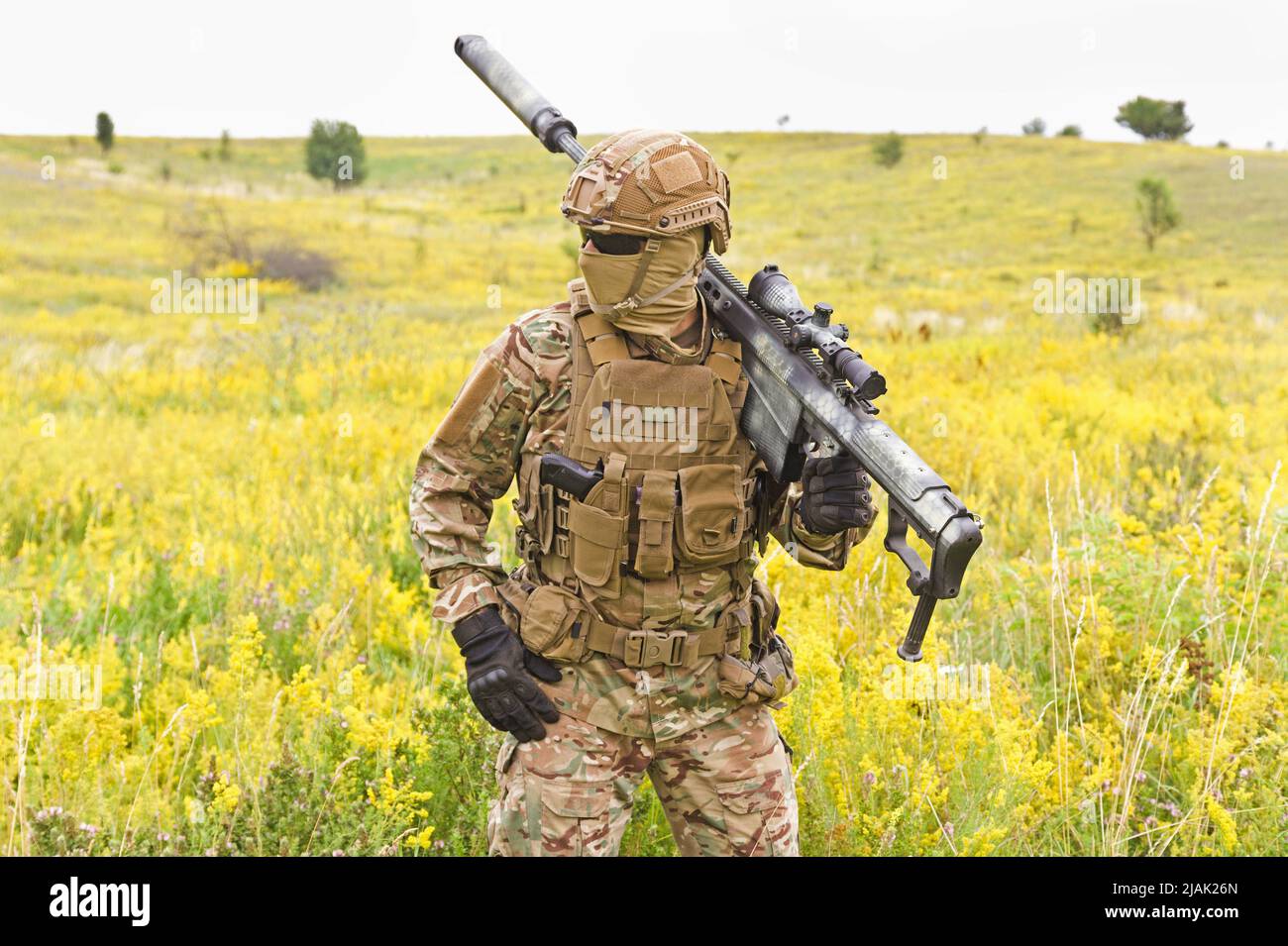 Soldier in a special military uniform, carrying a sniper rifle in a field. Stock Photo