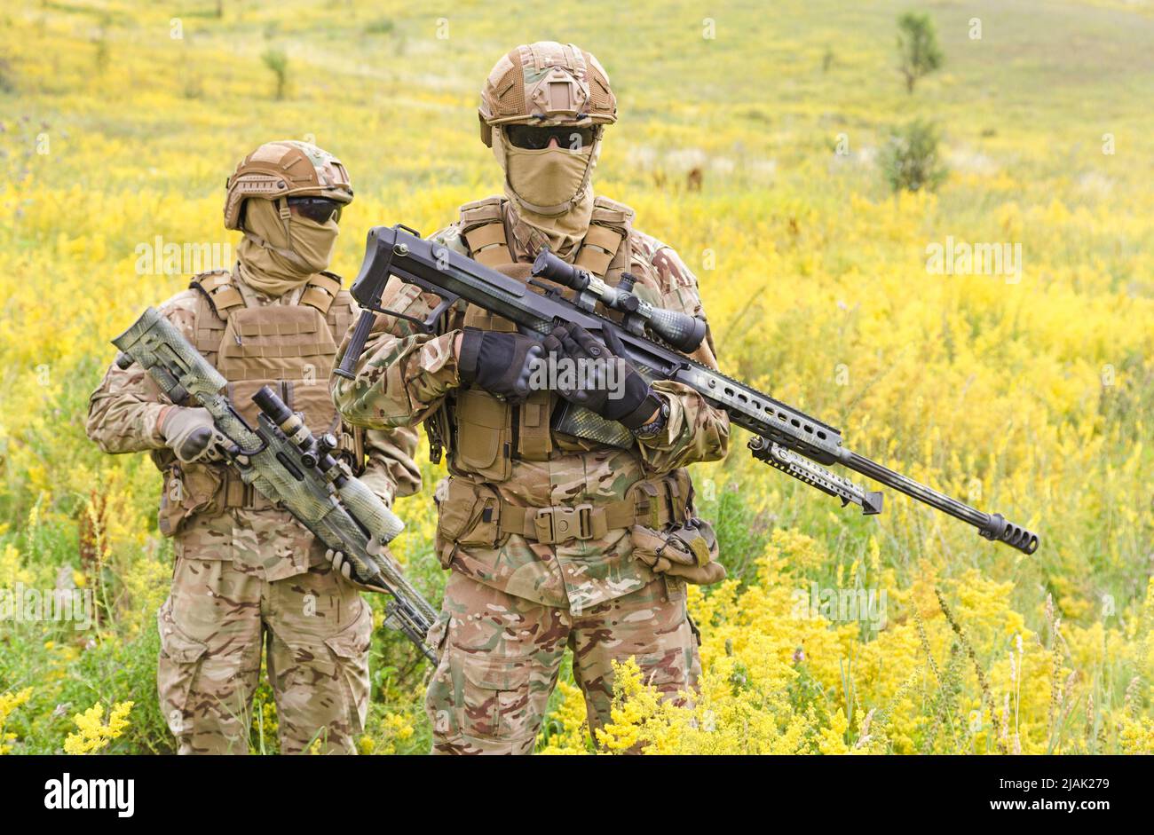 Two armed special forces soldiers with sniper rifles standing in a blooming field. Stock Photo