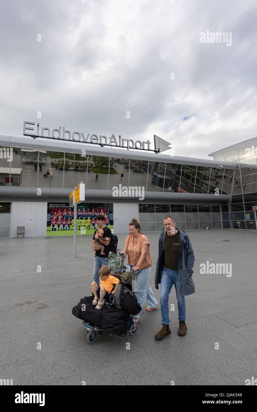 Family of tourist passengers with trolley and suitcases outside Eindhoven airport. Child sitting on bags and man holding baby Stock Photo