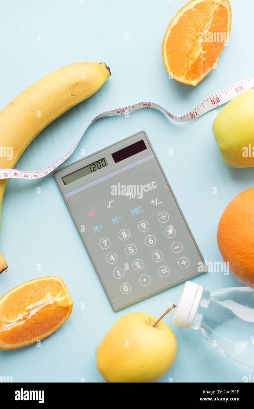 Calculator with numbers 1200, bottle of water, measuring tape and fruits on blue background