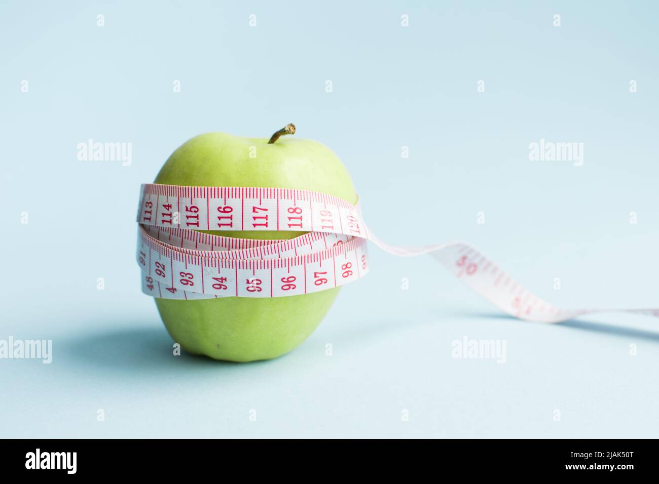 Apple with measuring tape on blue background. Weight loss, counting