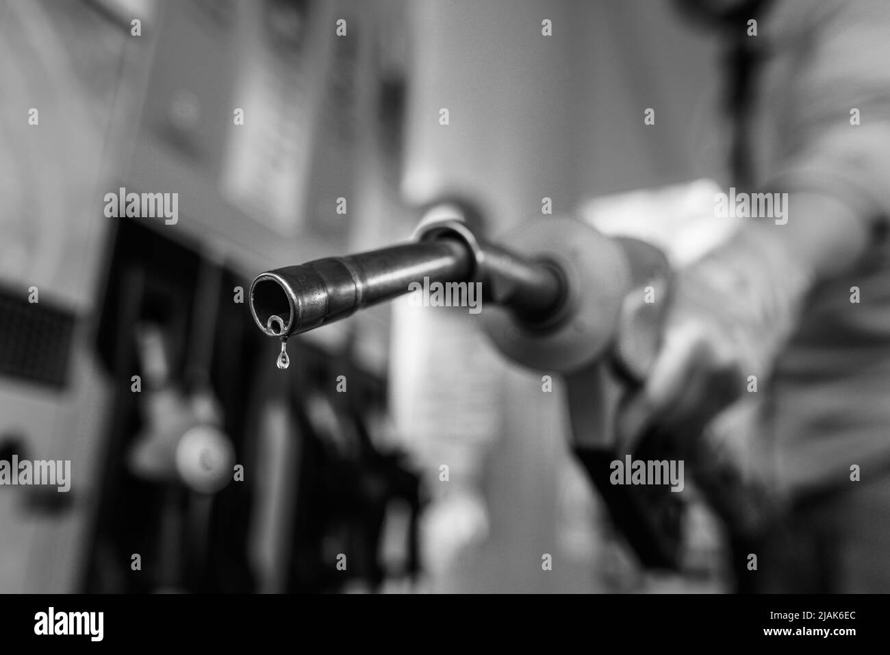 Shallow depth of field (selective focus) details with a man holding a fuel pump dripping with gasoline in a gas station. Stock Photo