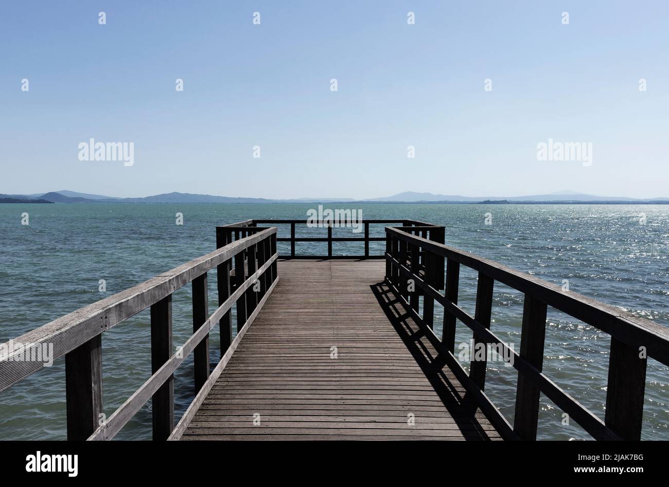 Long wooden pier on lake  Trasimeno , Italy , in the background coastline Stock Photo