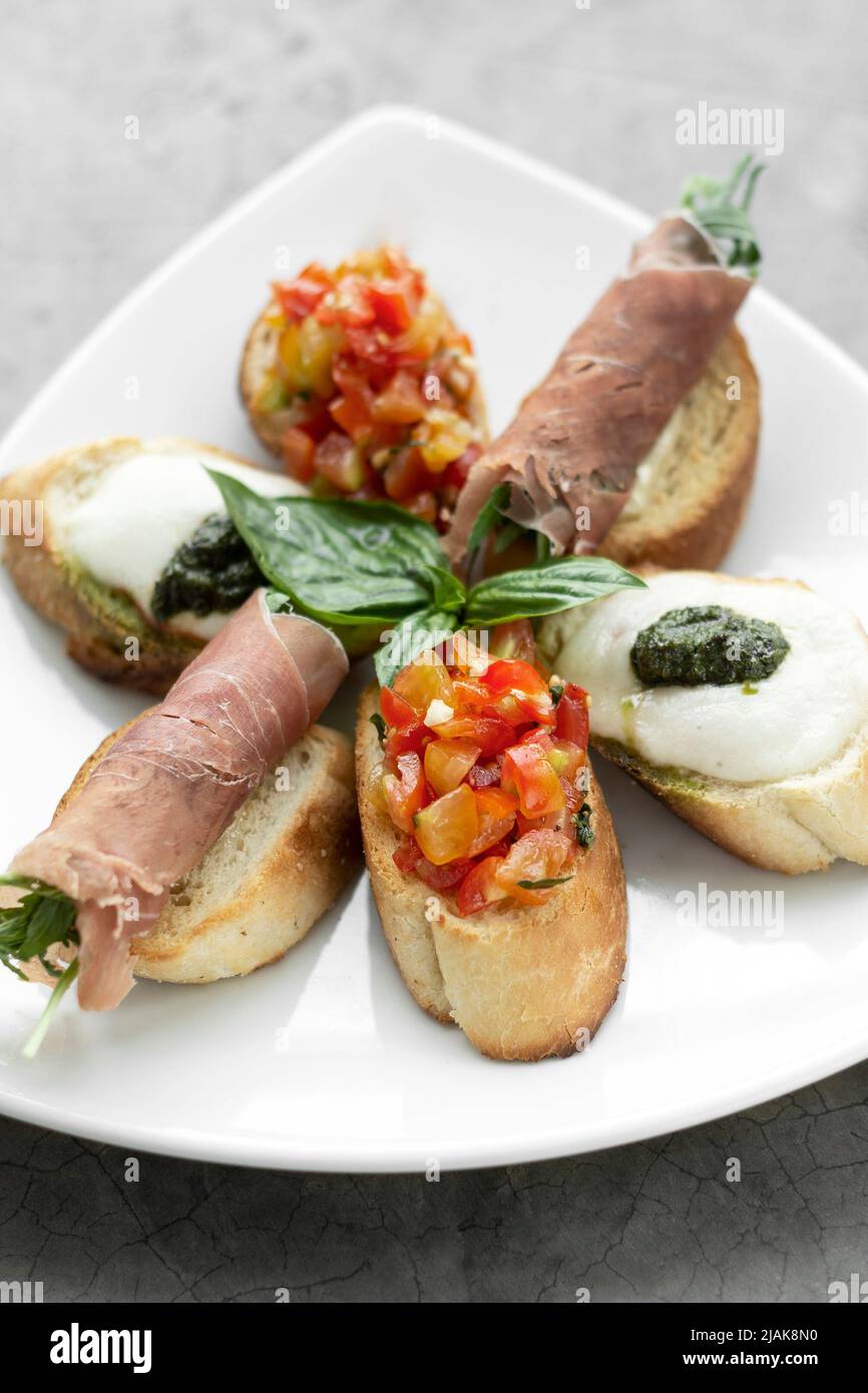 mixed crostini appetizers with parma ham, bruschetta and mozarella toppings Stock Photo