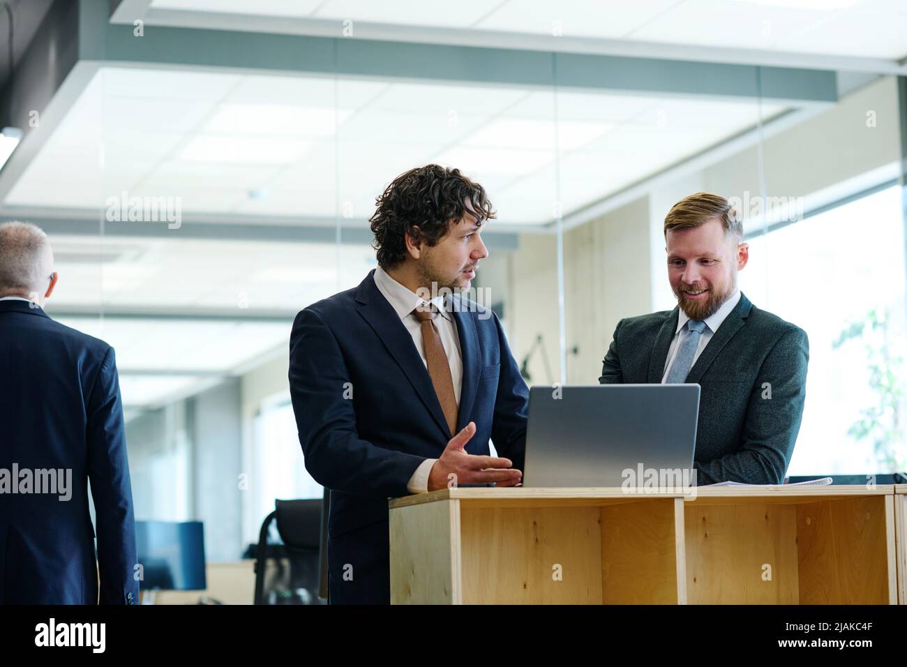 Two business partners in suits discussing new software on laptop together at office Stock Photo