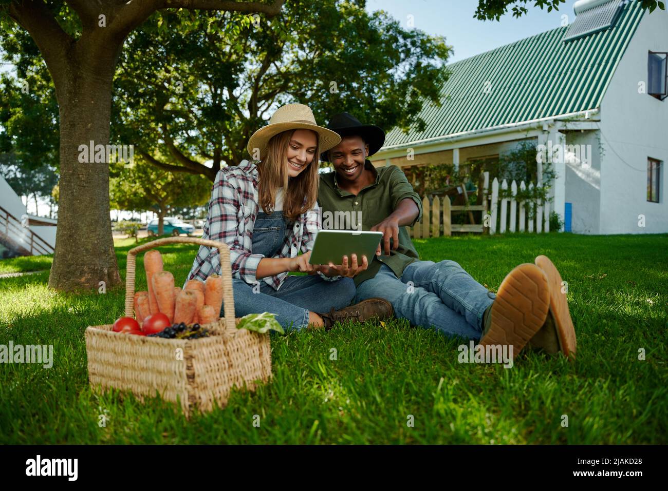 Mixed race male and female farmers sitting on green grass researching for research project Stock Photo