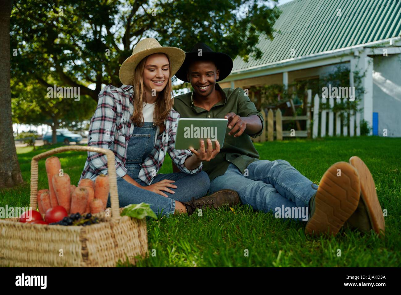 Mixed race male and female farmers sitting on green grass researching for school project  Stock Photo