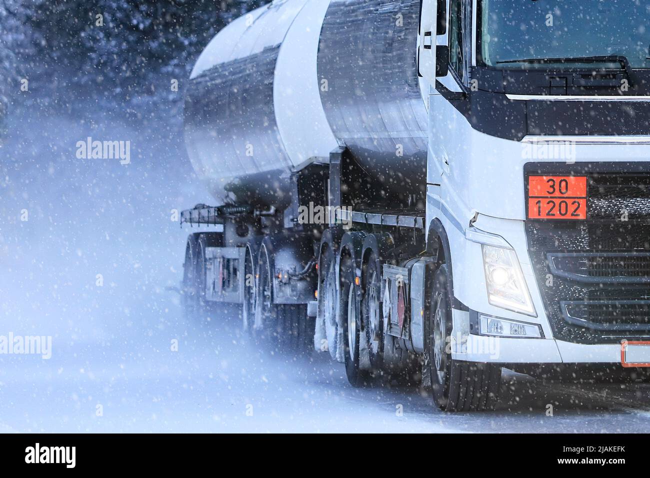 Detail of a white tanker truck transporting diesel oil, ADR 30-1202, along road in heavy snowfall. Stock Photo