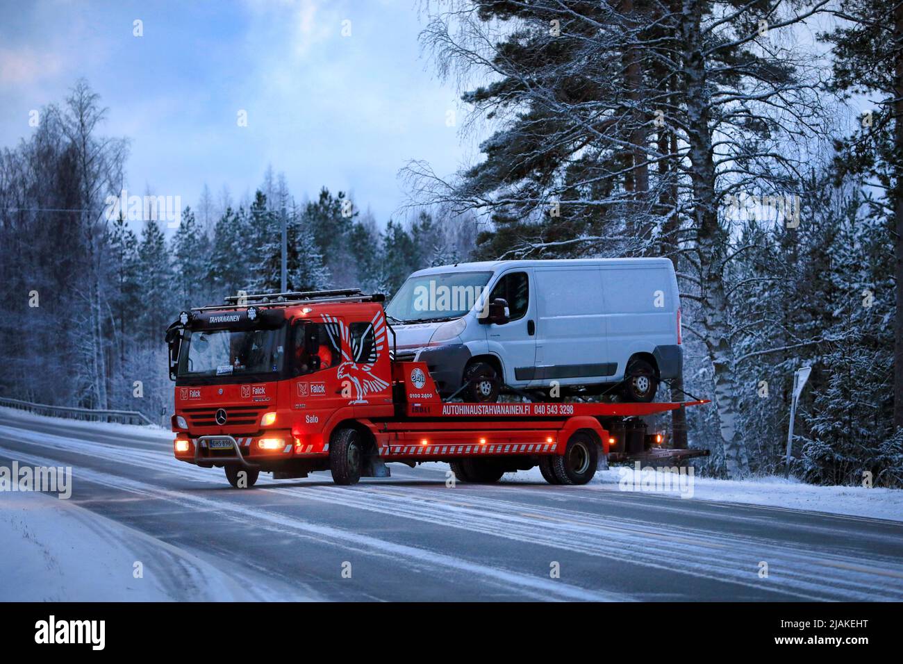 Mercedes-Benz Atego tow truck carrying a white van enters highway on a winter evening. Salo, Finland. December 28, 2021. Stock Photo
