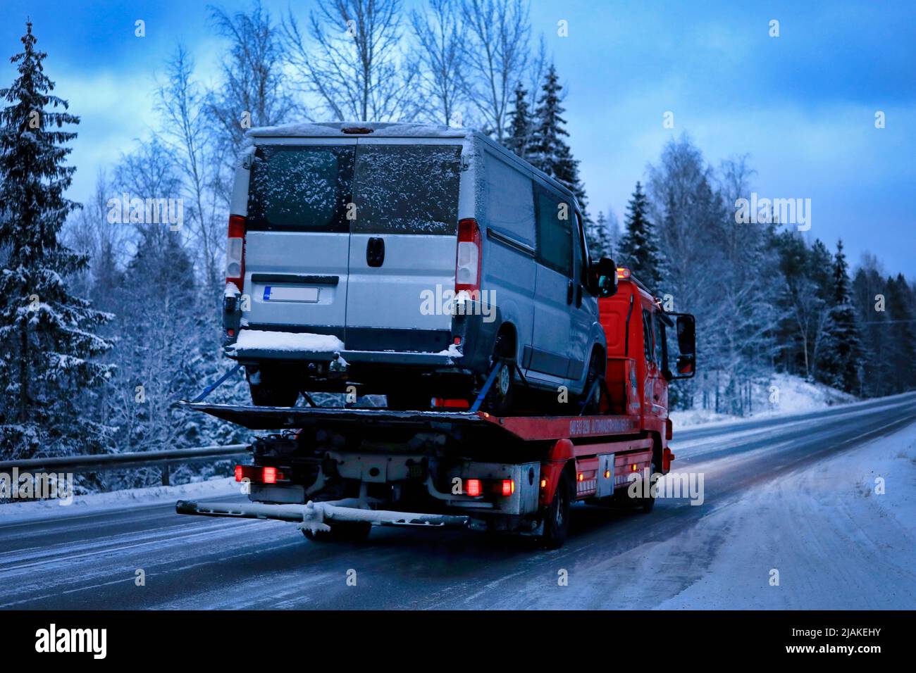 Mercedes-Benz Atego tow truck carrying a van at speed on highway on a winter evening, rear view. Salo, Finland. December 28, 2021. Stock Photo