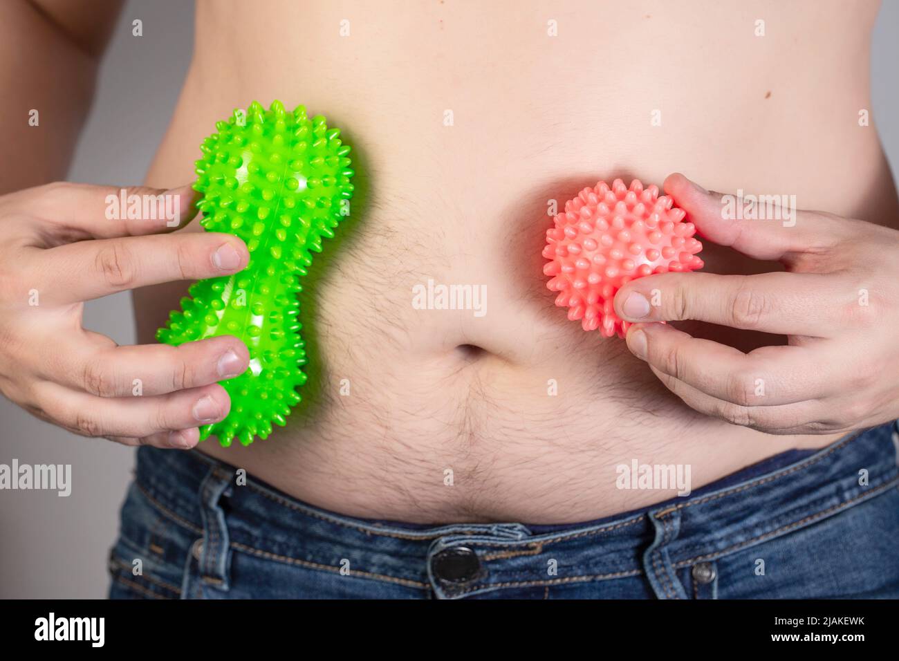A man holds two anti-cellulite massagers against the background of a fat belly. Burning fat with procedures. Fast weight loss. Stock Photo