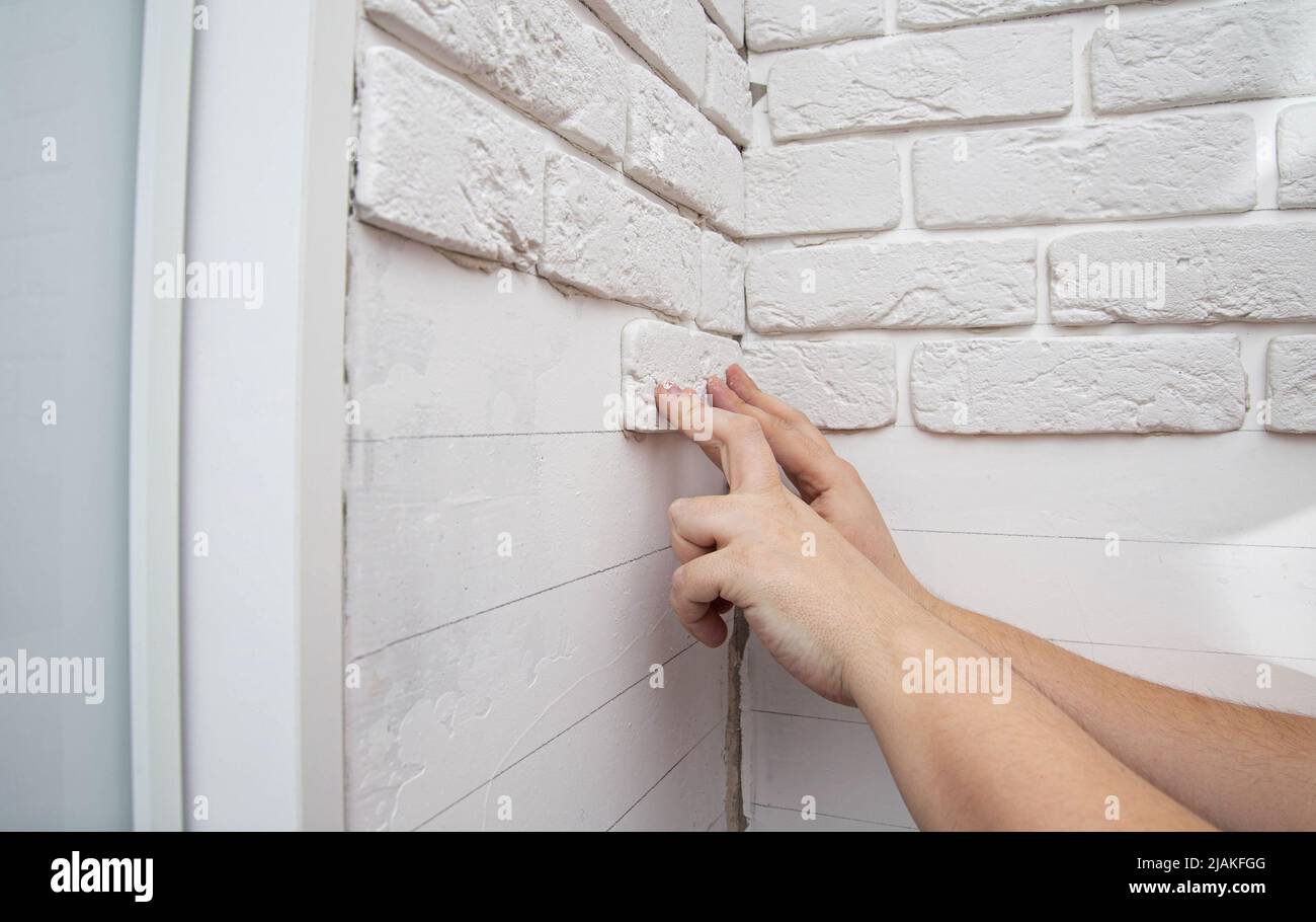 A man glues a white decorative stone in the form of a brick to the wall. Decor element, copy space for text Stock Photo