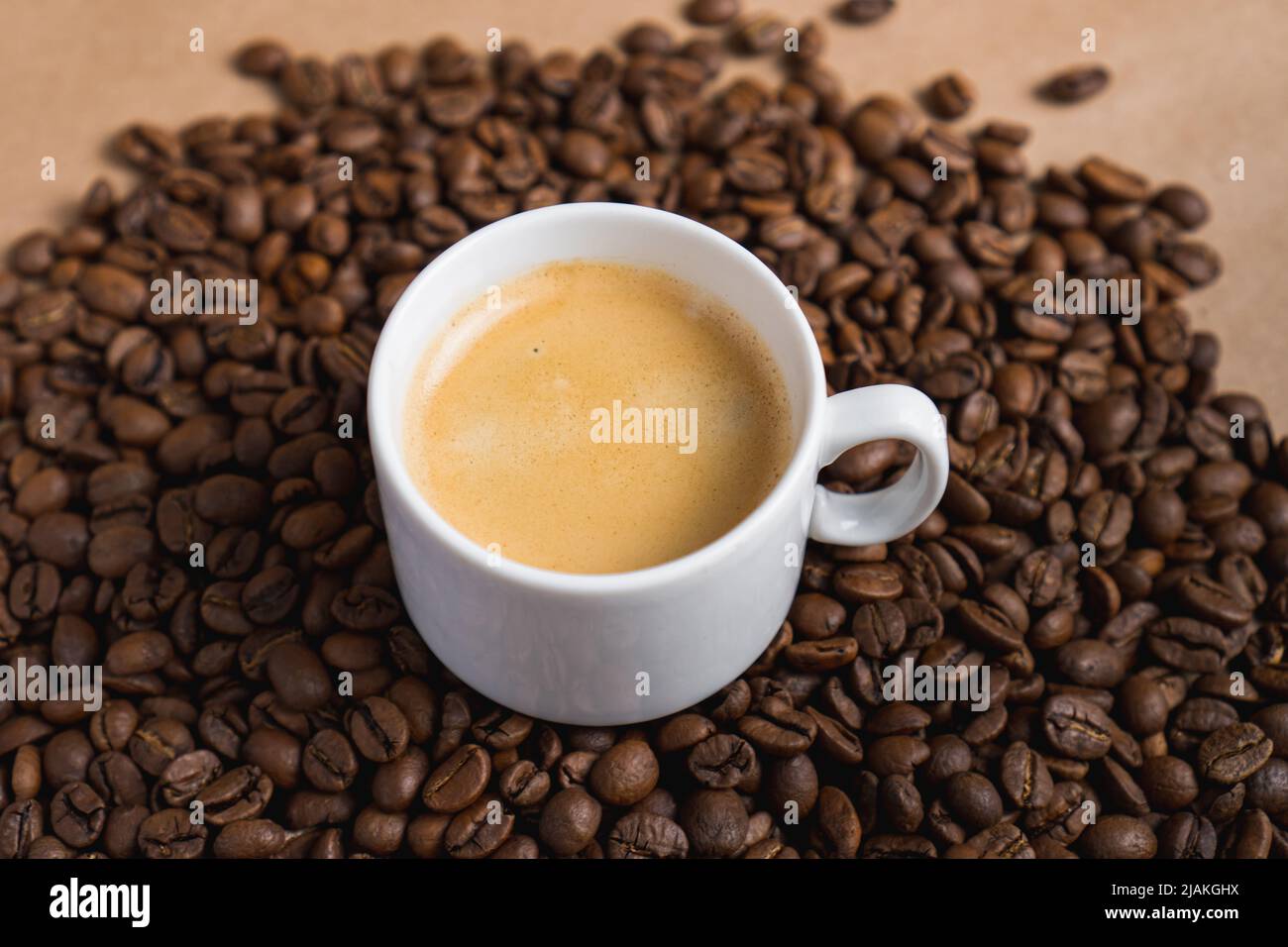 Small white coffee cup with espresso crema on roasted beans at brown