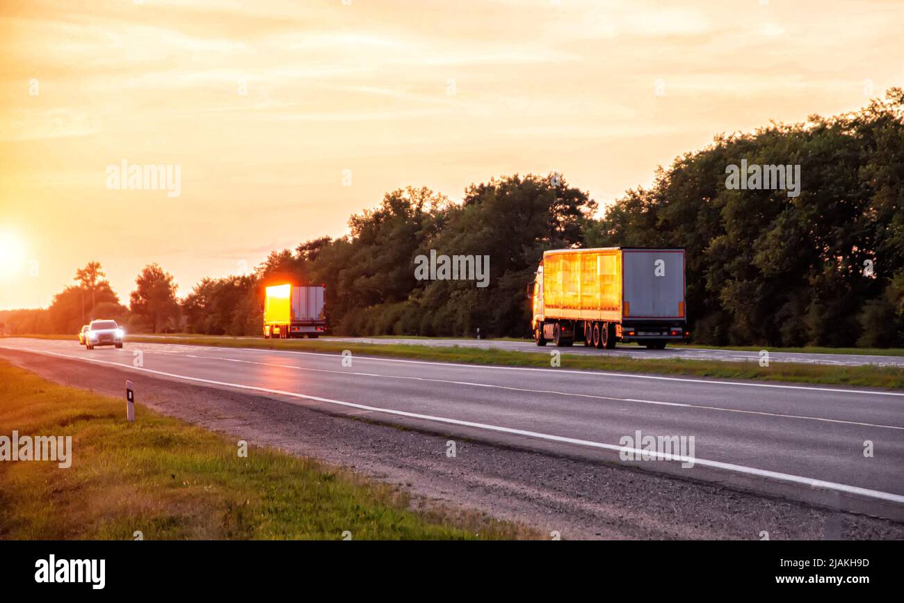 a convoy of trucks delivers cargo along the highway in the evening at sunset. The concept of cargo transportation and logistics companies FTL, truckin Stock Photo