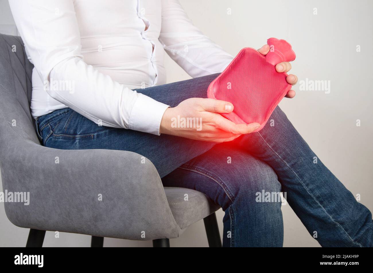 A male office worker holds a heating pad with hot water near the knee