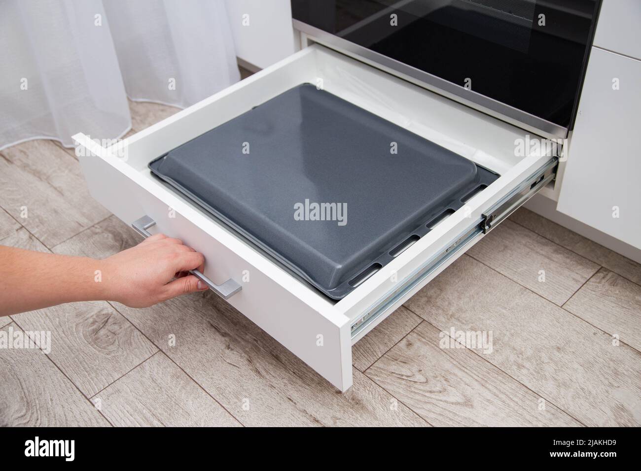 A man pulls out a drawer with baking sheets in the kitchen. A special