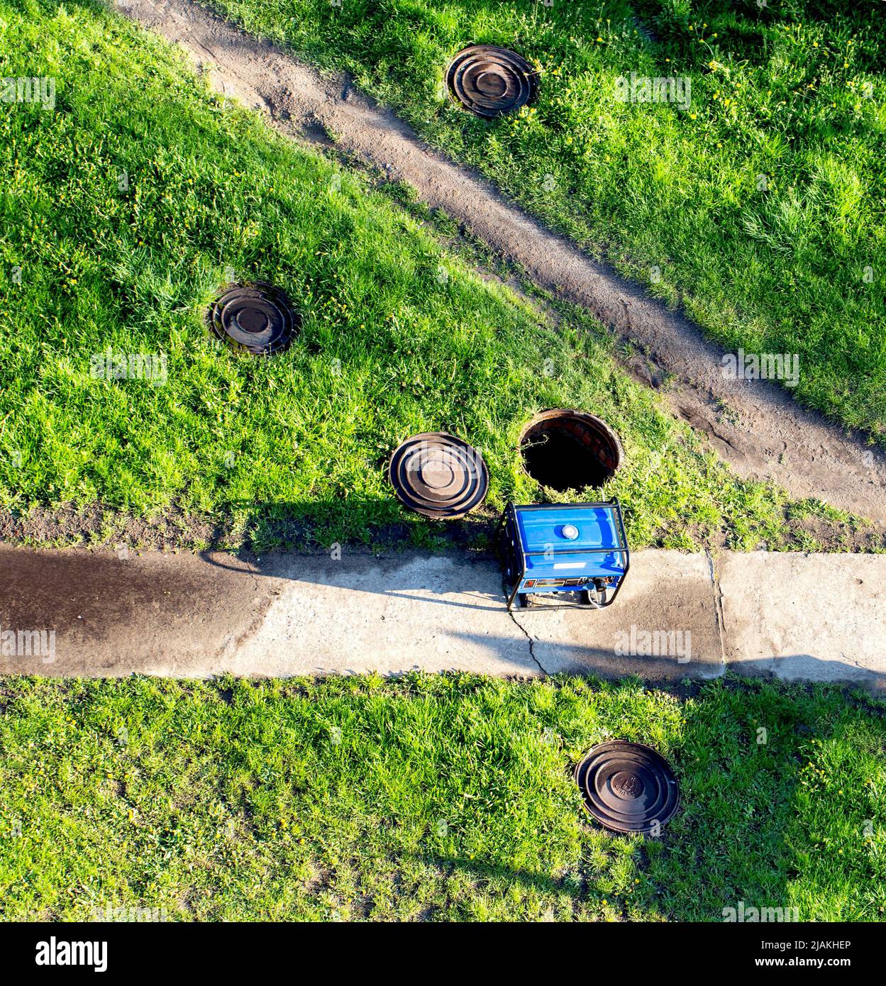 An open sewer well near which there is a gas generator on the grass. The concept of repair and maintenance of inspection and sewer wells. Accident in Stock Photo