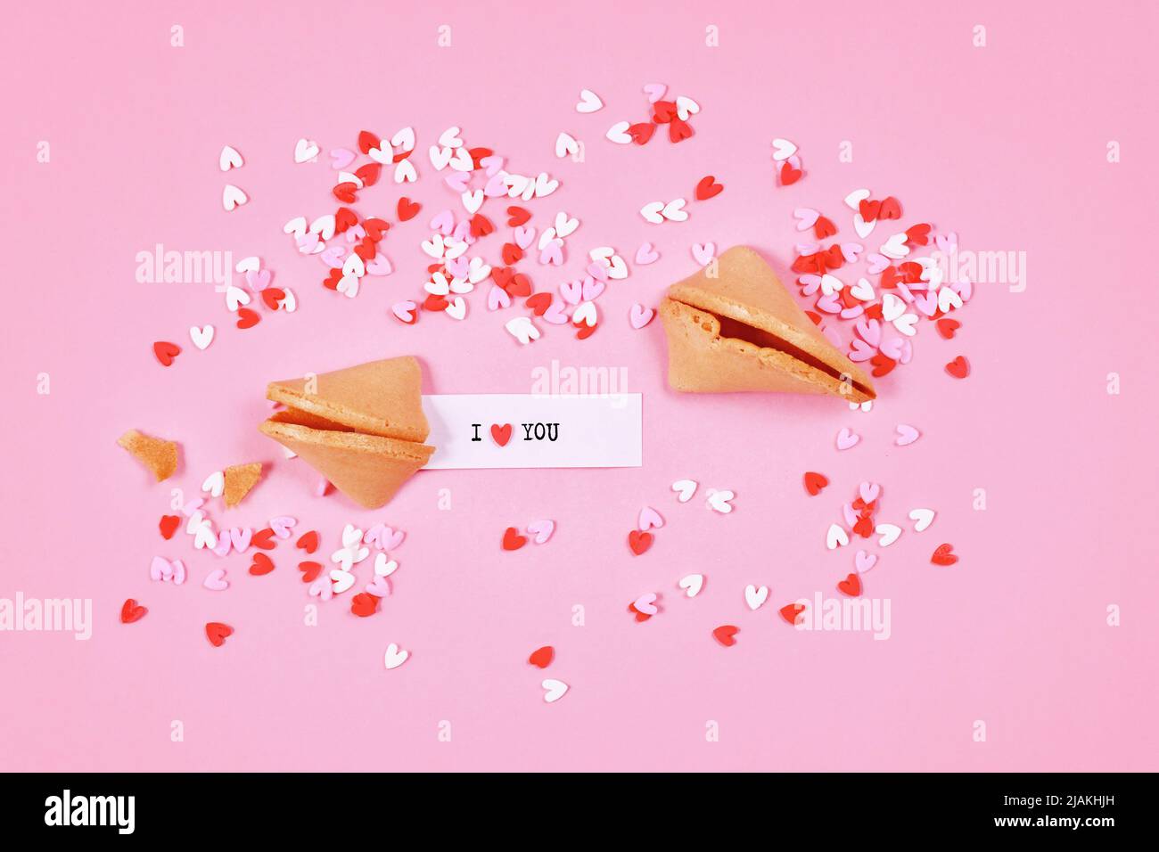 Fortune cookies with text 'I love you' and sugar sprinkle hearts on pink background Stock Photo