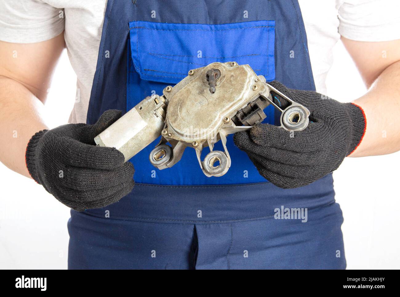 A car mechanic holds a broken electric windshield wiper motor in his hands against the background of a blue overalls. Repair and replacement of car pa Stock Photo