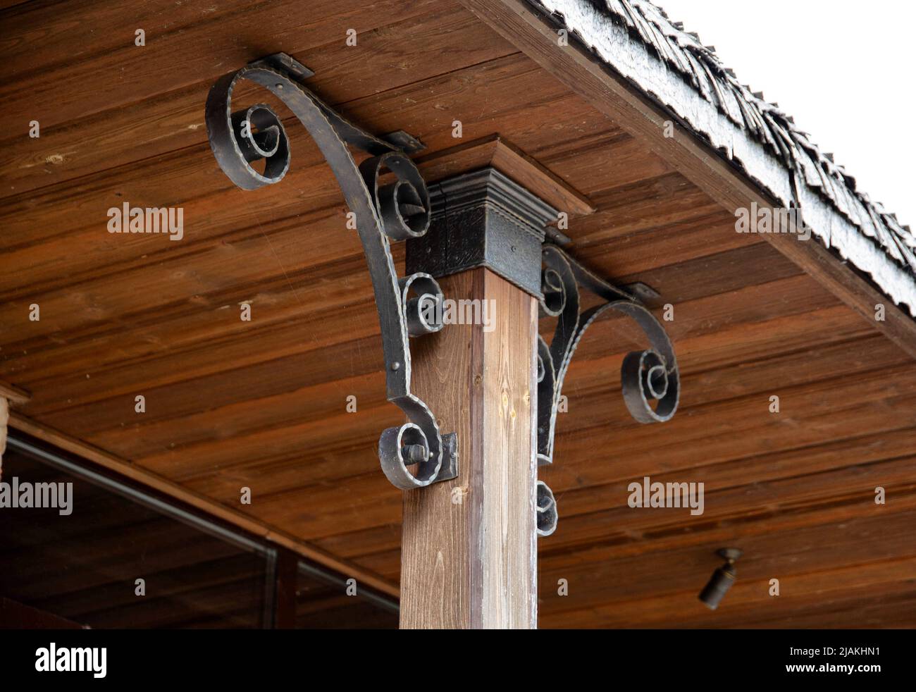 A metal corner decoration that holds the roof of the house and a wooden pillar post. Vintage design Stock Photo